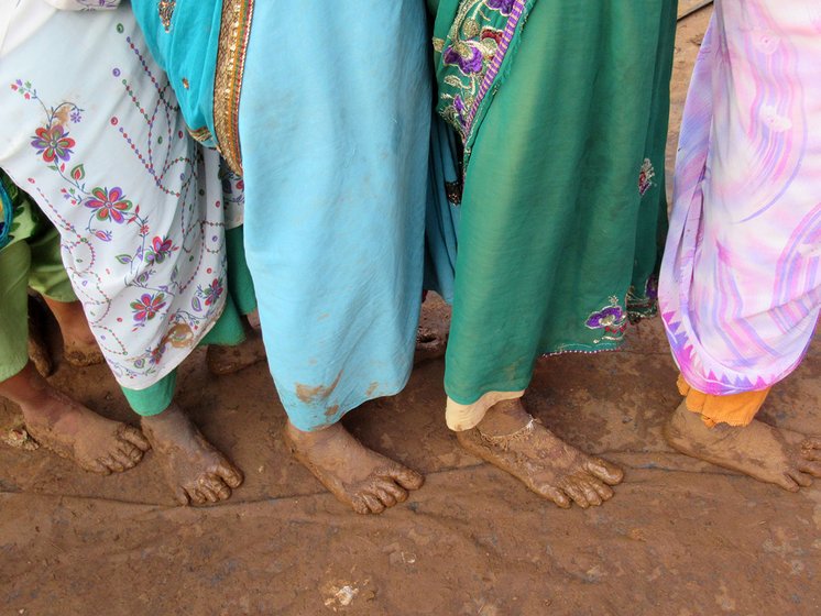 A group of women standing with bare feet on a muddy ground