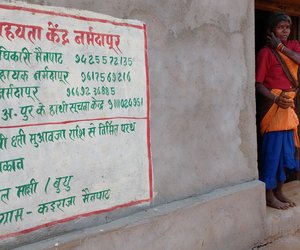 Adivasi woman standing next to wall with warning sign